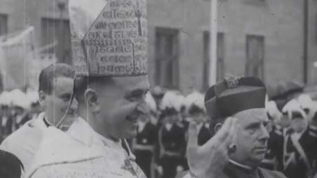 German Catholic Newsreel Black and white photograph: close-up of Archbishop Aloysius Muench in clerical dress and pointed bishop's mitre, inscribed with medieval script. Standing next to him is a cardinal wearing a cardinal's cap.