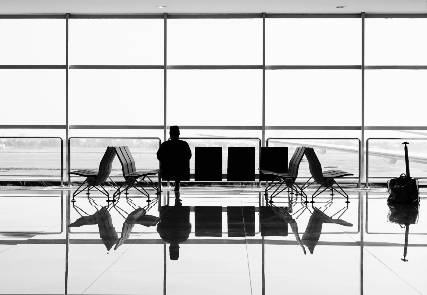 Allein wartender Reisender mit Gepäck in einer Flughafenhalle / Lone traveller waiting with luggage in an airport departure lounge