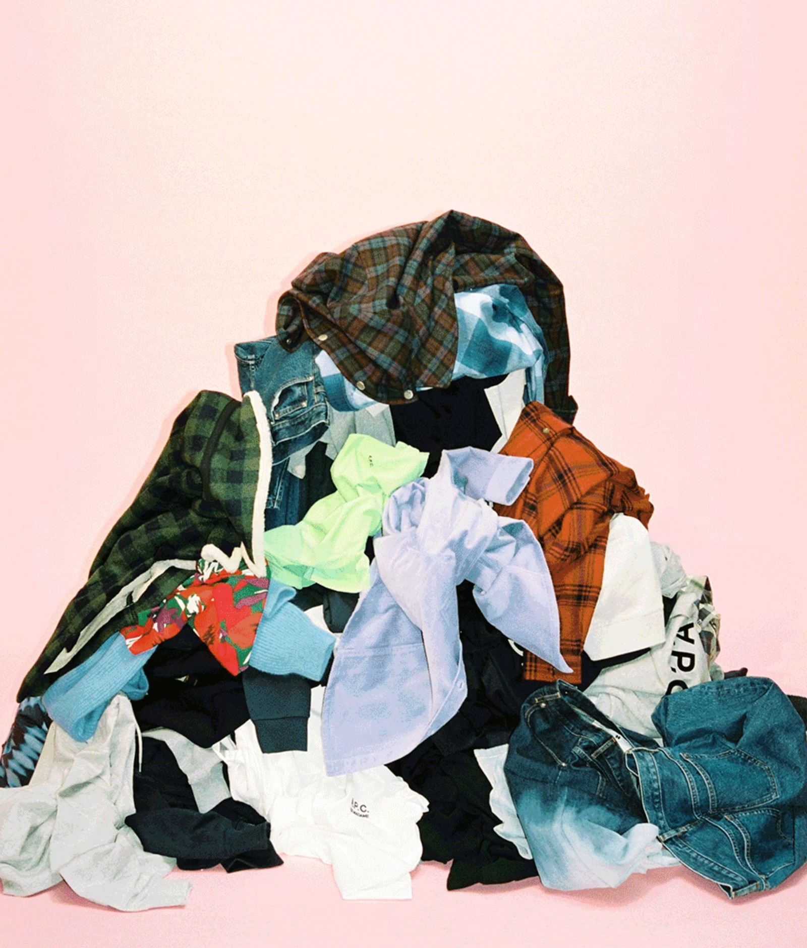 Pile of assorted colorful clothes, including shirts, jeans, and jackets, heaped on a light pink background.