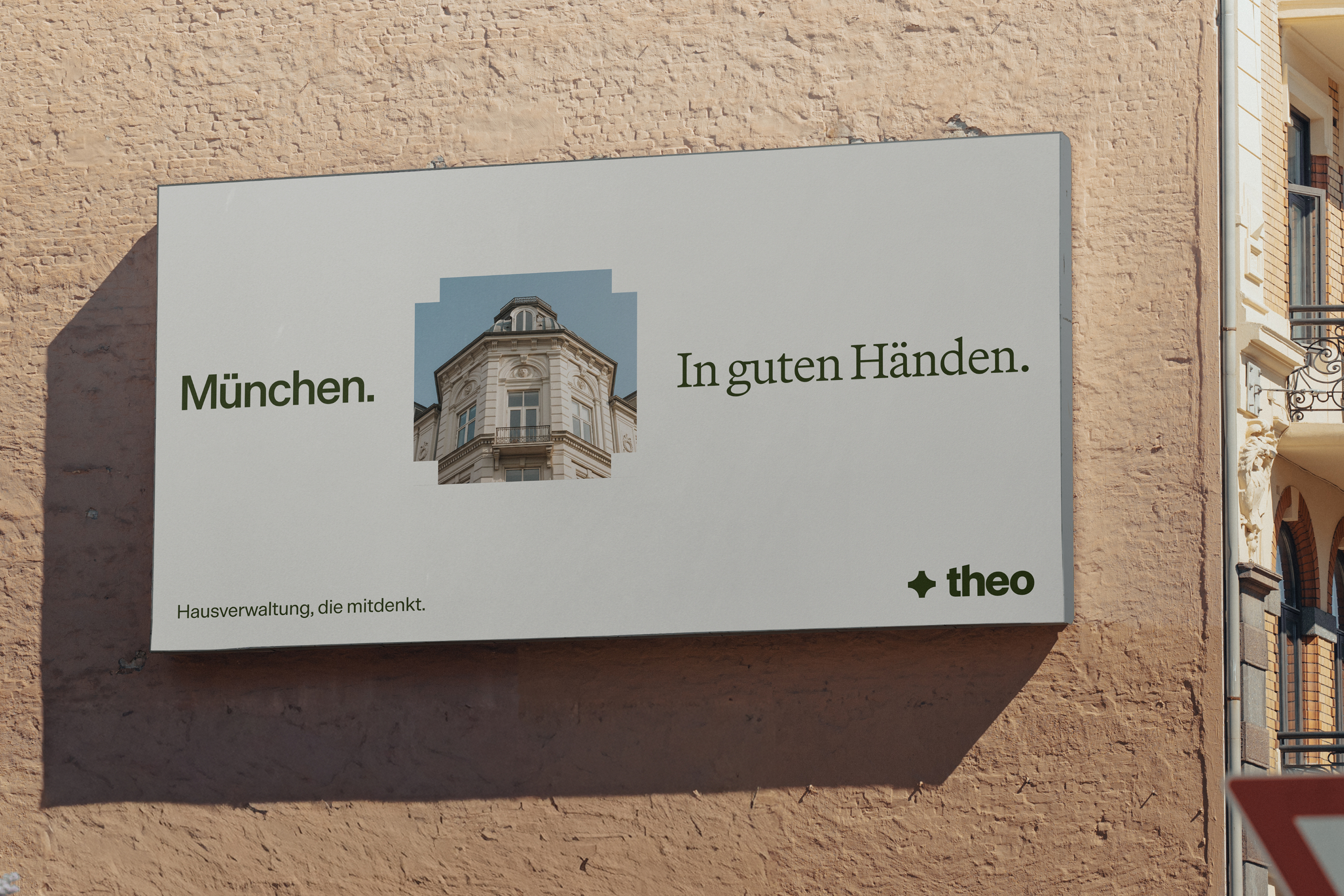 Large Theo billboard on a brick wall featuring a historic building and the German text “München. In guten Händen.”