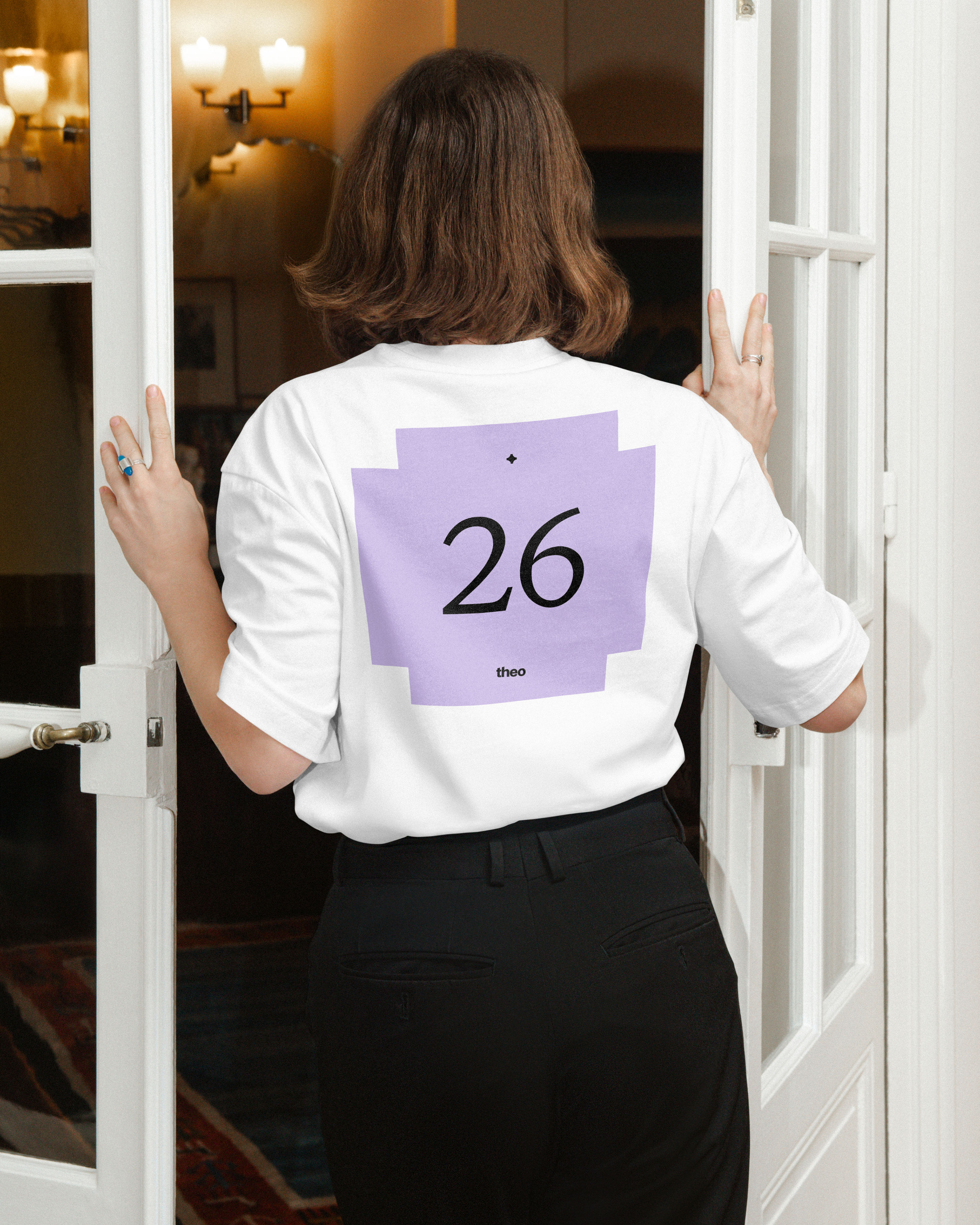 Rear view of a person entering a doorway in a white T-shirt with a purple graphic featuring the number 26 and the word theo.