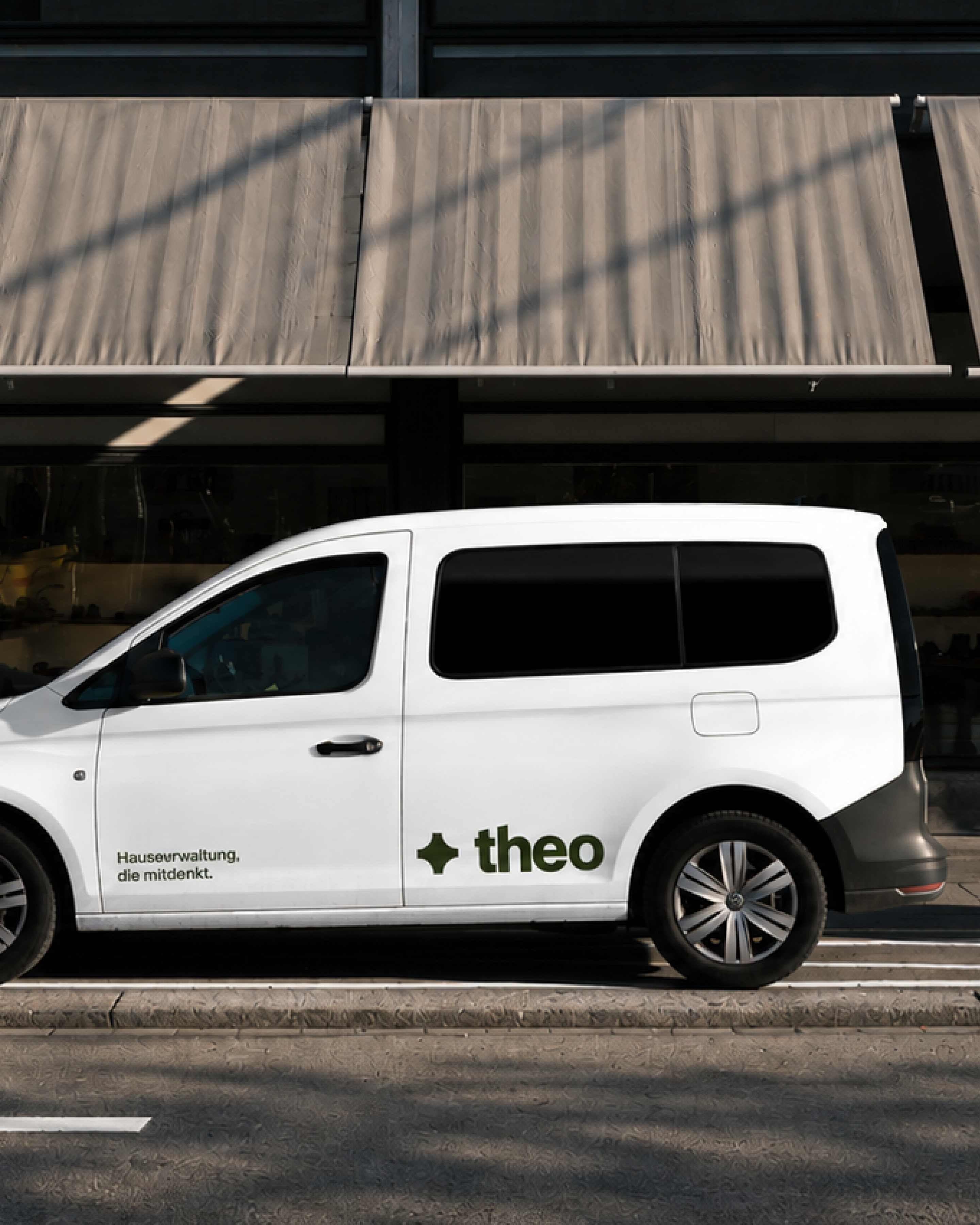 White Theo-branded utility van parked outside a modern building with fabric awnings.