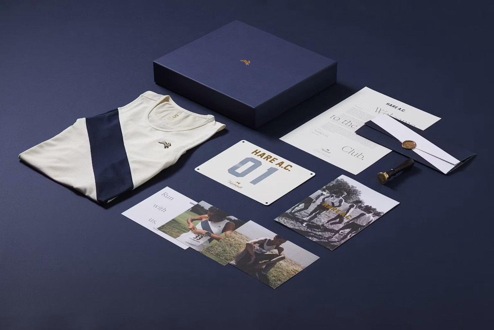 Flat lay of a folded cream running singlet, navy box, race bib, photos, and printed stationery arranged neatly on a dark blue surface.