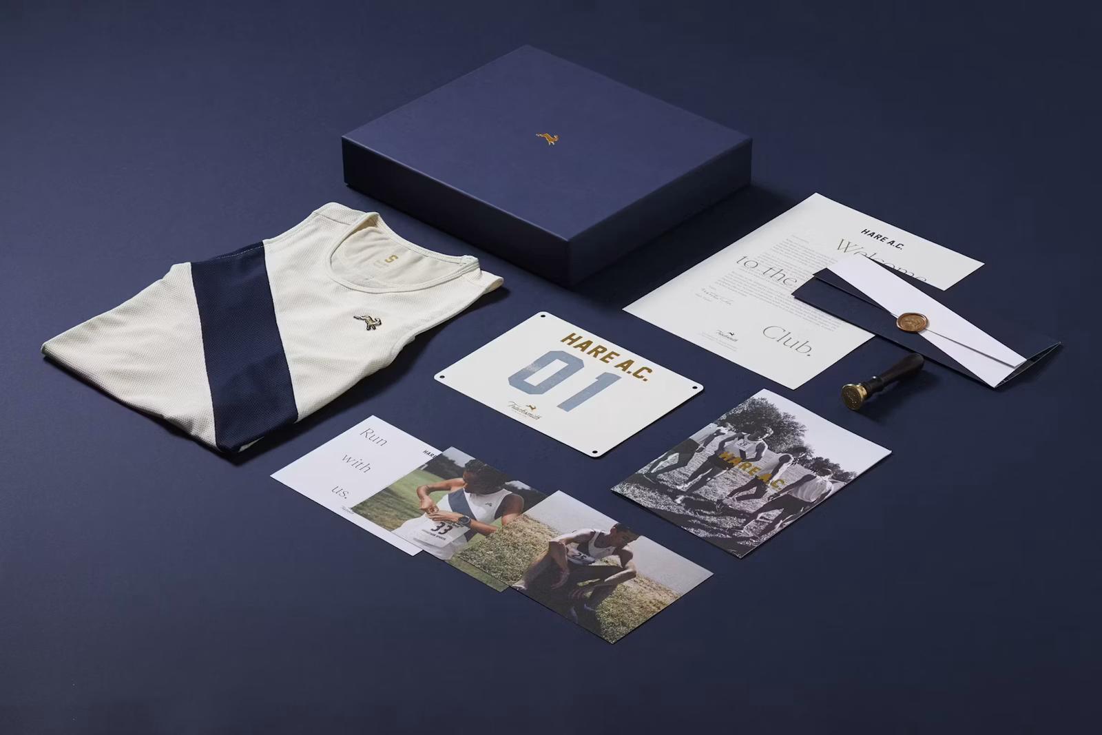 Flat lay of a folded cream running singlet, navy box, race bib, photos, and printed stationery arranged neatly on a dark blue surface.
