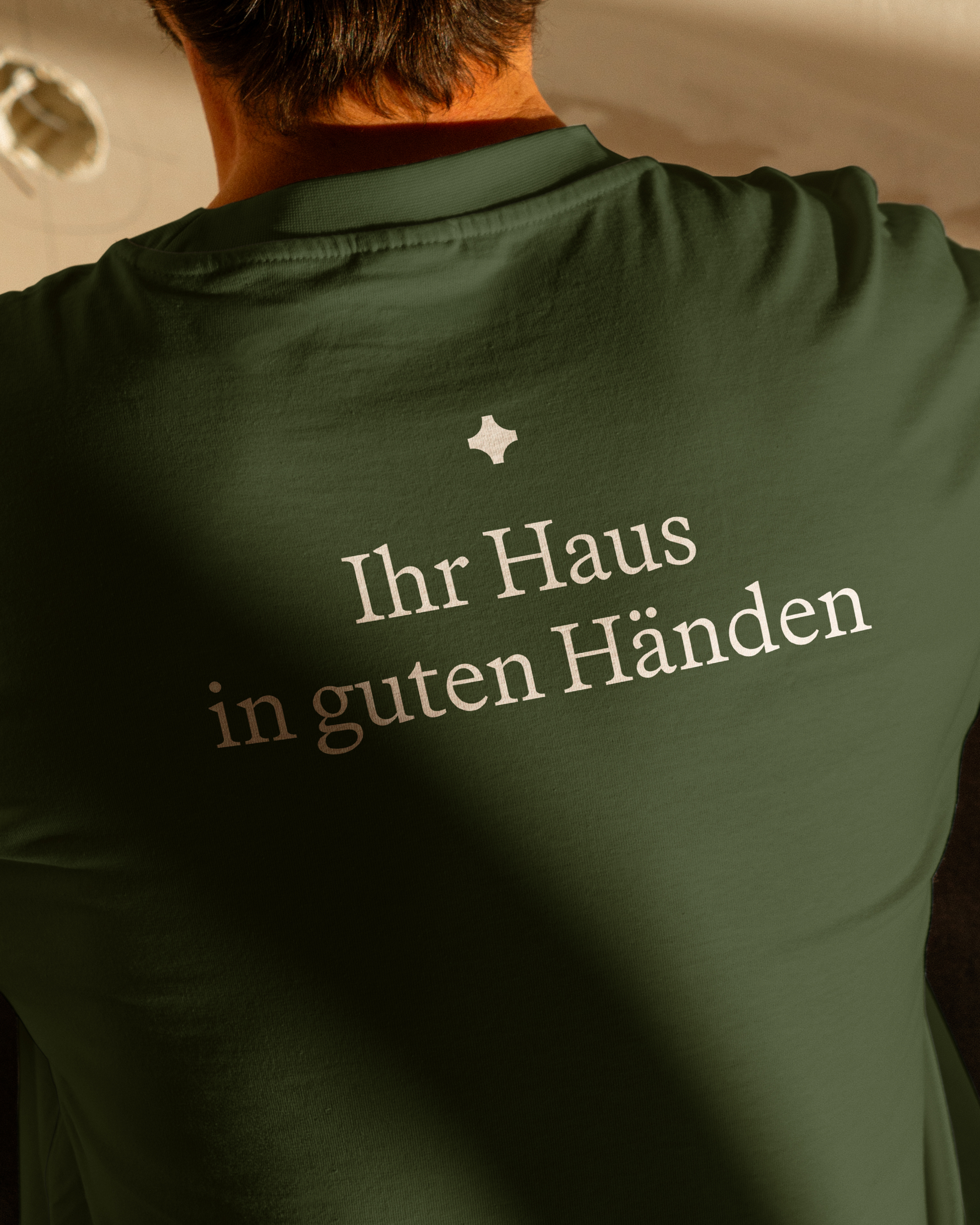 Close-up from behind of a person wearing a dark green shirt with white German text and a small white symbol.