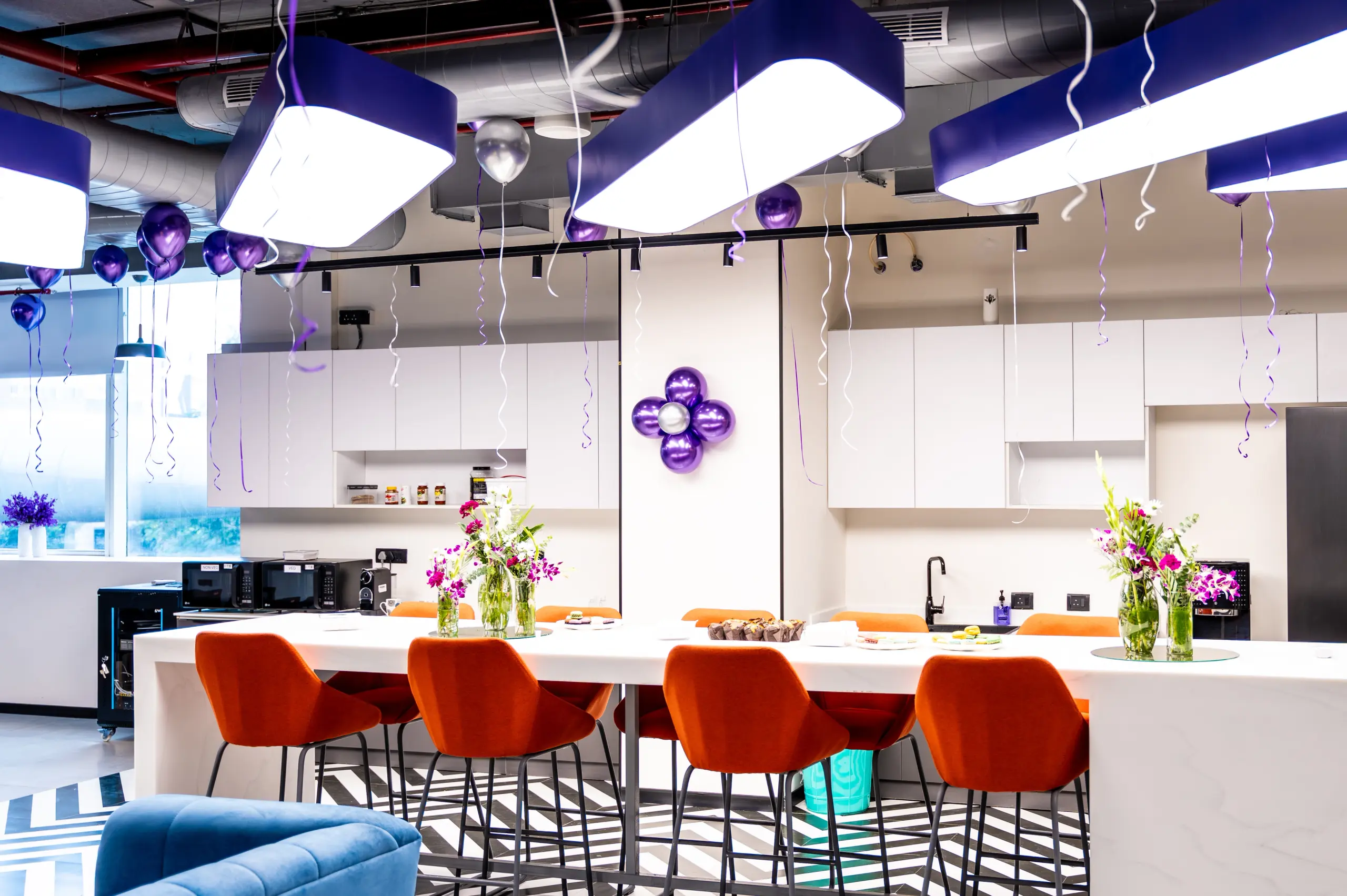 A modern office breakroom decorated with purple balloons and streamers