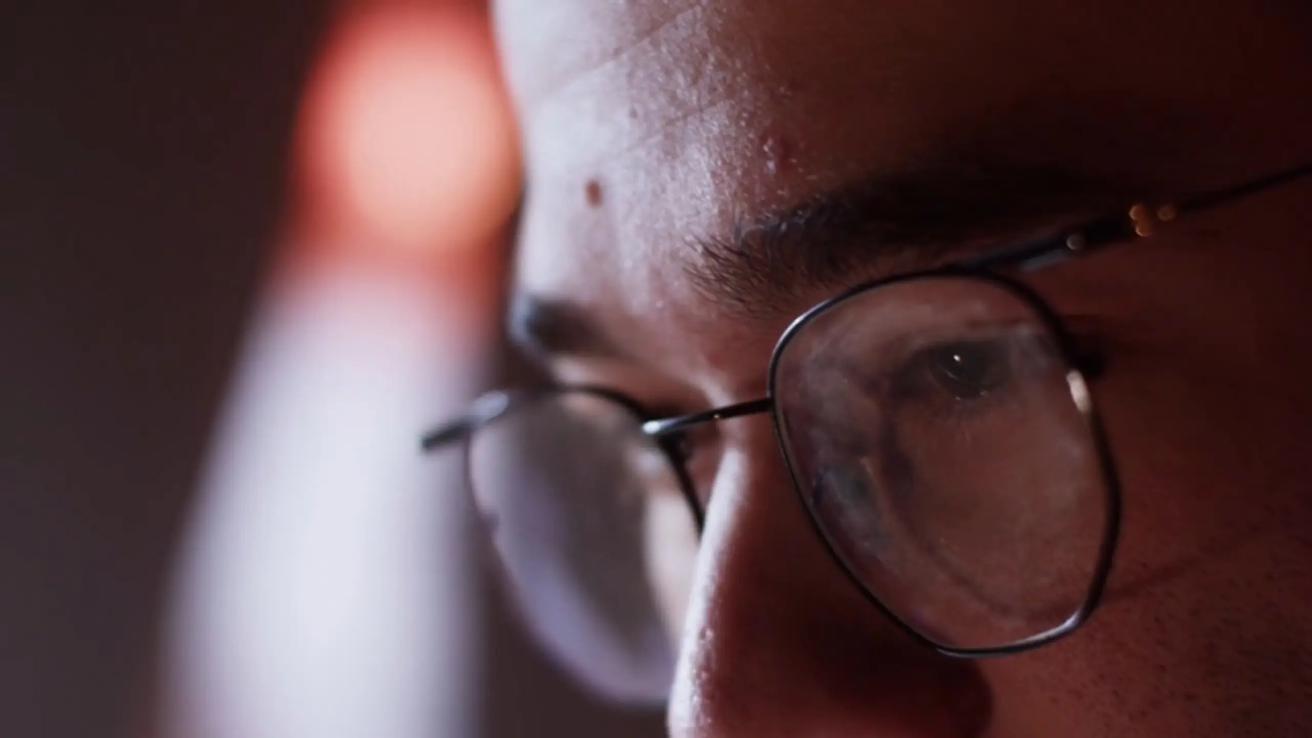 Close-up of a person's eye behind glasses, reflecting a screen.