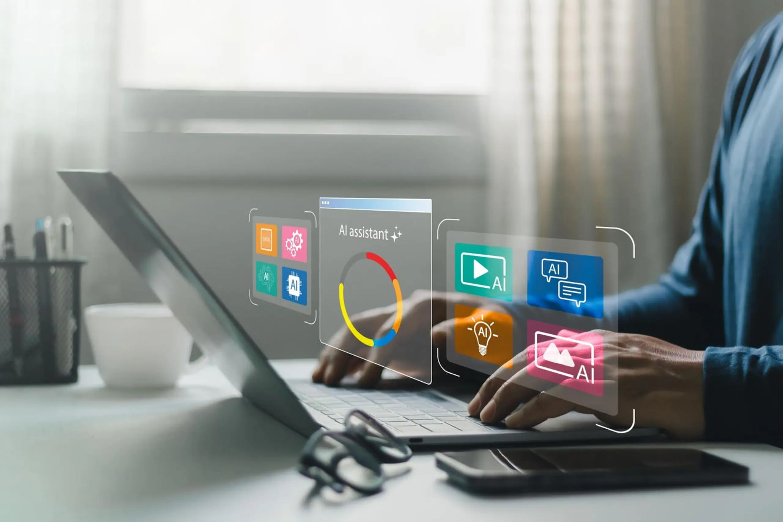 A person uses a laptop, interacting with a holographic AI assistant interface featuring various colorful icons.