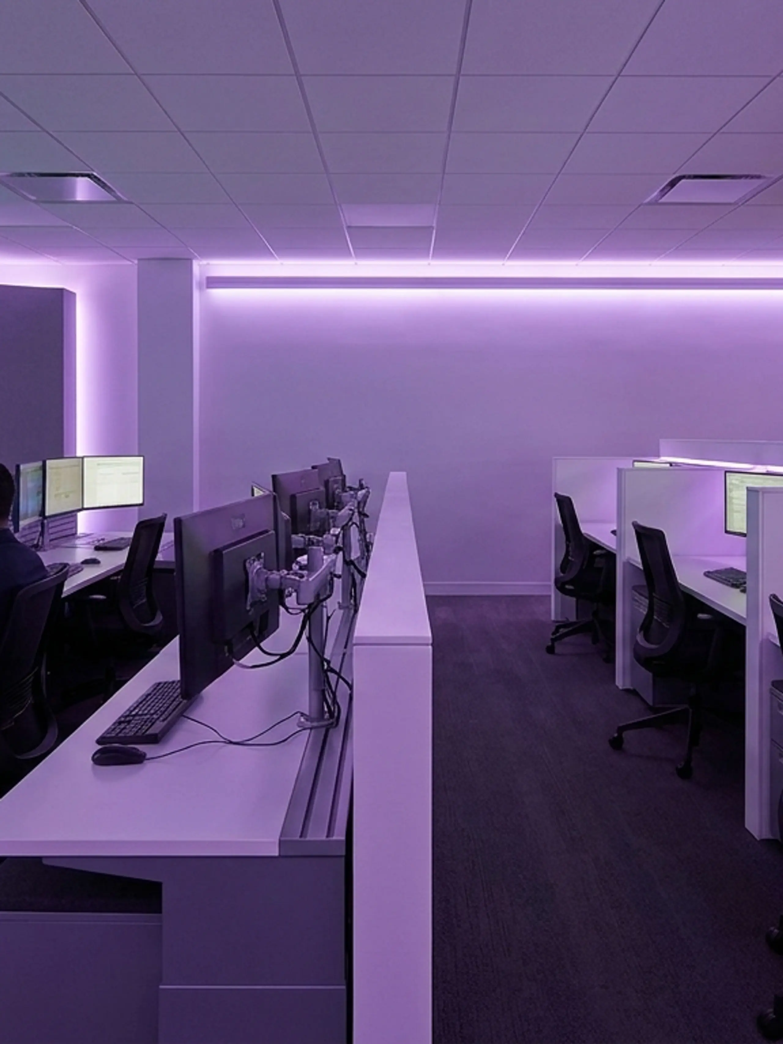 People working in a modern control room with purple ambient lighting and multiple computer screens displaying data.