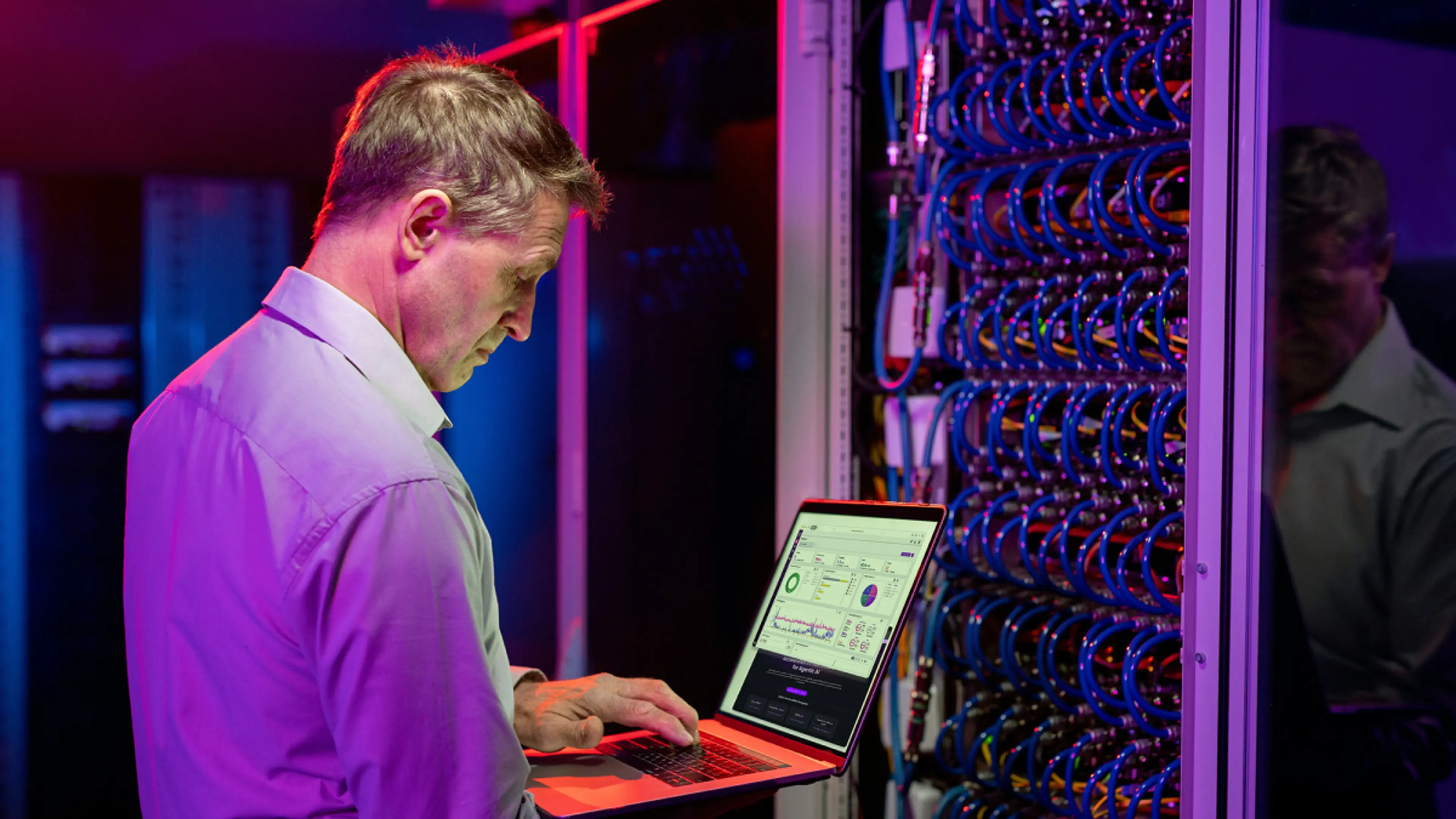 A man works on a laptop in a data center.
