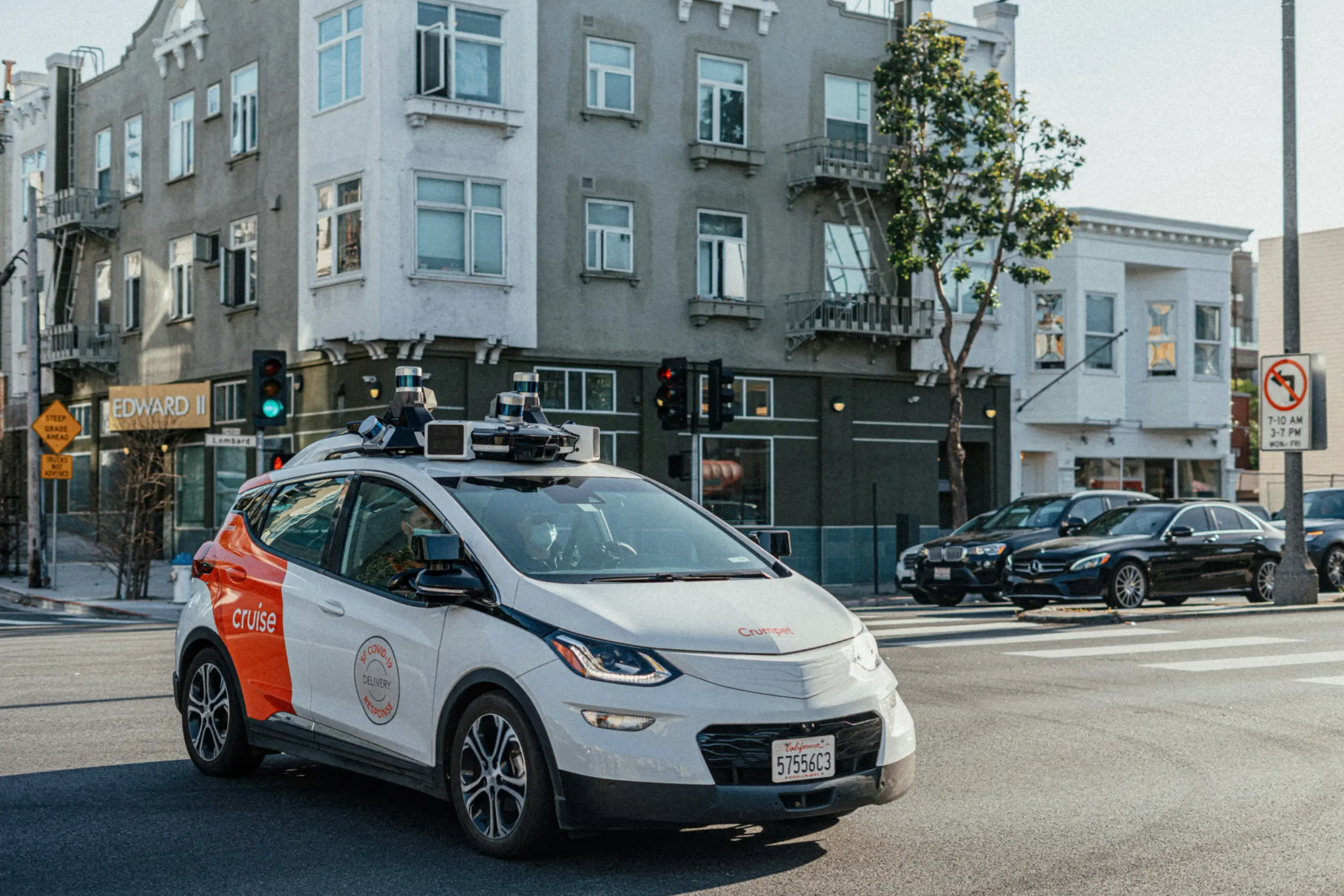 A white and orange Cruise autonomous vehicle with roof sensors on a city street.