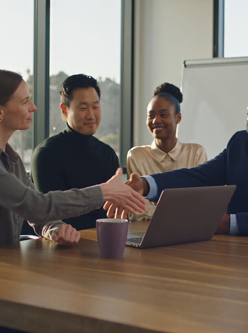 Diverse business professionals shaking hands across a laptop at a meeting.