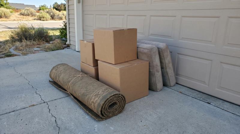 Bulk trash staged on a driveway beside a closed garage door at a home in Star, Idaho, with a rolled rug, stacked boxes, and old couch cushions ready for pickup.
