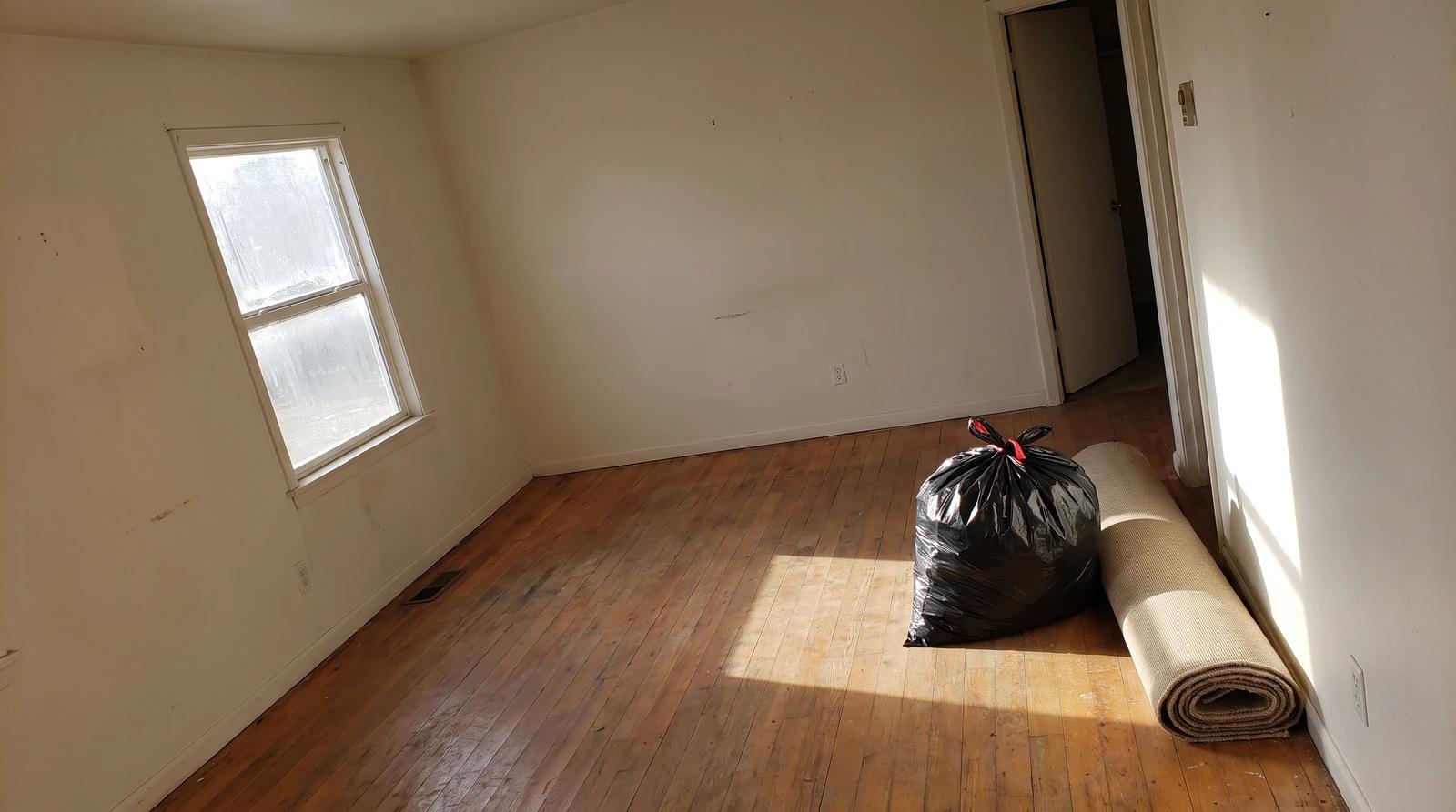 Empty living room of a rental home in Garden City, Idaho after a property cleanout, with a trash bag and rolled rug by the door