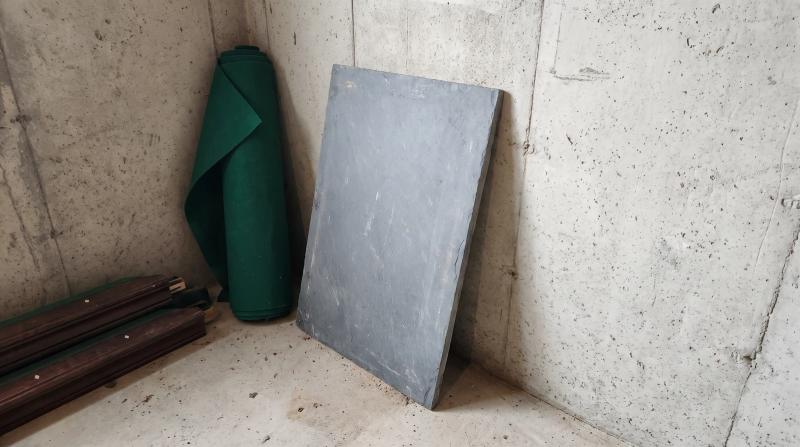 Gray slate slab, rolled green felt and wooden rails stacked against a basement wall after pool table removal at a home in Boise, Idaho.