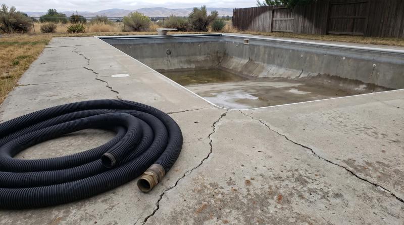 A drained in-ground backyard pool with an empty concrete shell ready for demolition at a home in Kuna, Idaho.