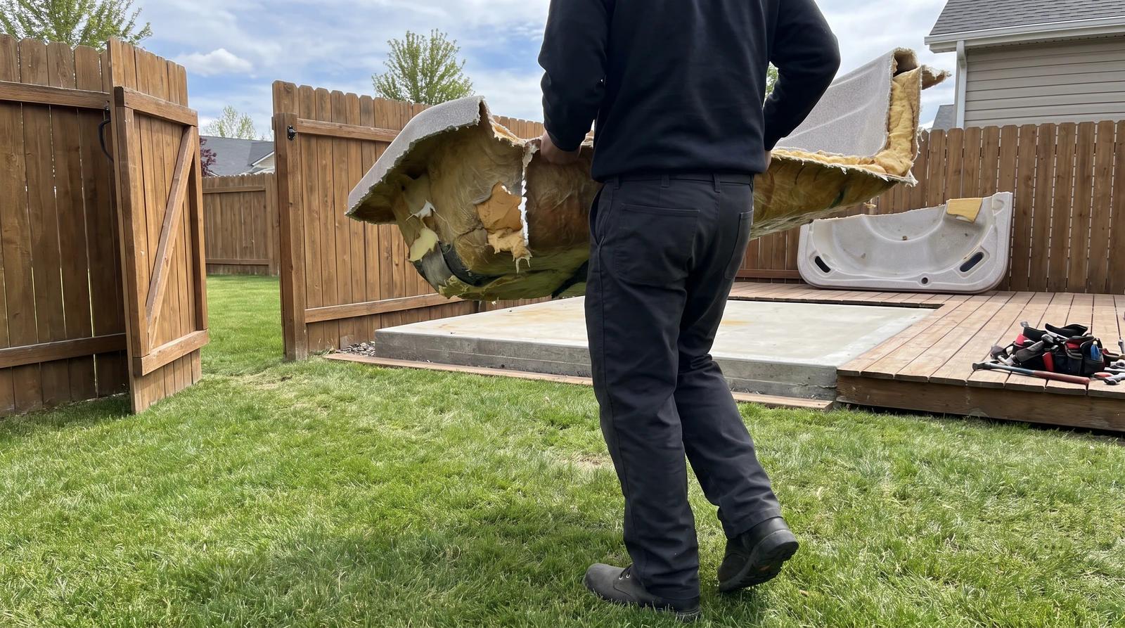 Worker carrying a cut piece of an old hot tub shell through a backyard gate during a hot tub removal in Star, Idaho