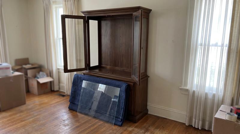 Empty wooden china cabinet with glass shelves wrapped in a moving blanket, ready for furniture removal from a dining room in Middleton, Idaho