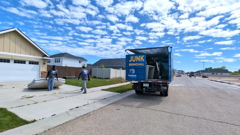 Two Top Shelf crew members in branded shirts carrying a mattress from a driveway to the truck in a Nampa Idaho subdivision