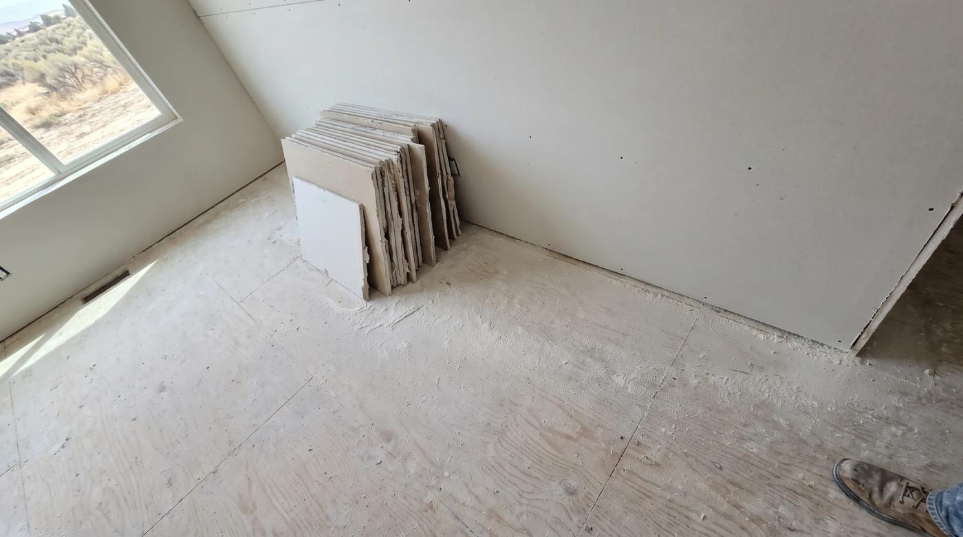 Drywall offcuts stacked in a neat pile inside an empty remodeled room in Eagle, Idaho, with fine construction dust settled on the bare subfloor