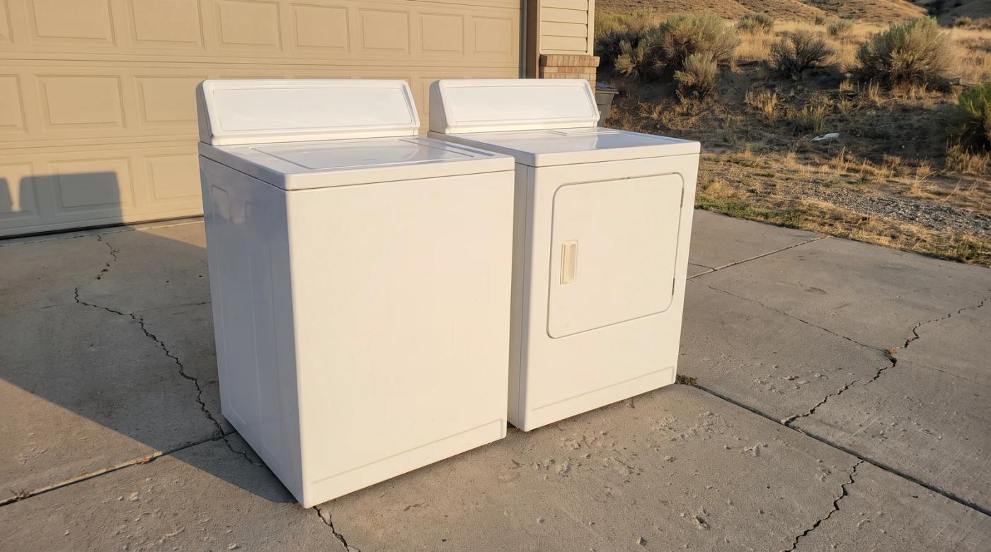 Plain white old washer and dryer side by side on a concrete driveway beside a closed garage door, waiting for appliance removal at a home in Star, Idaho