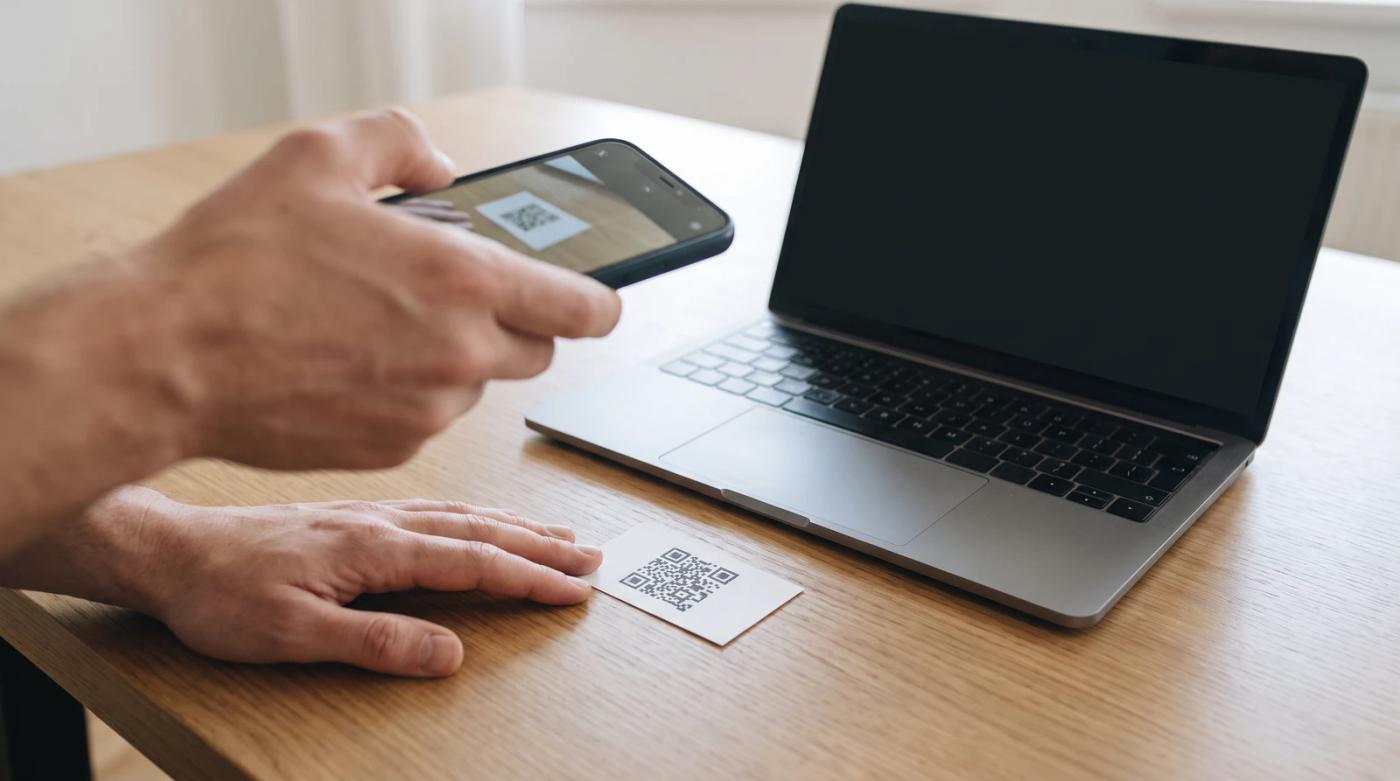 Business owner scanning a printed Google review QR code with a smartphone at a desk next to a laptop