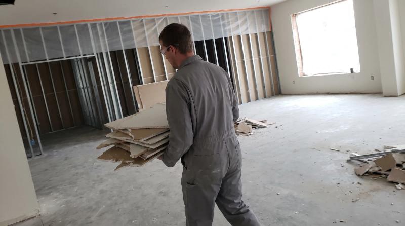 Worker clearing drywall from a sealed-off commercial unit during an interior demolition job in Middleton, Idaho