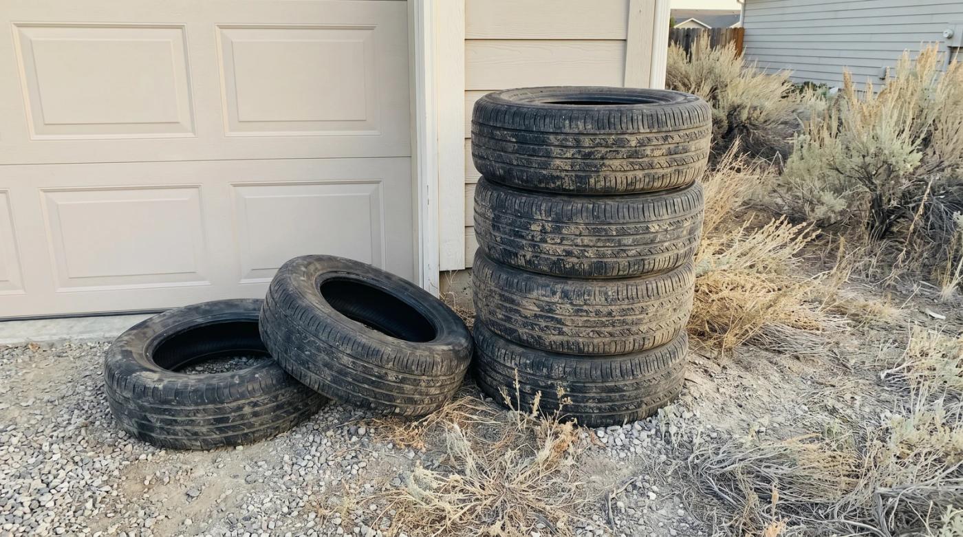 Stack of worn studded snow tires waiting on a gravel driveway beside a garage in Garden City, Idaho