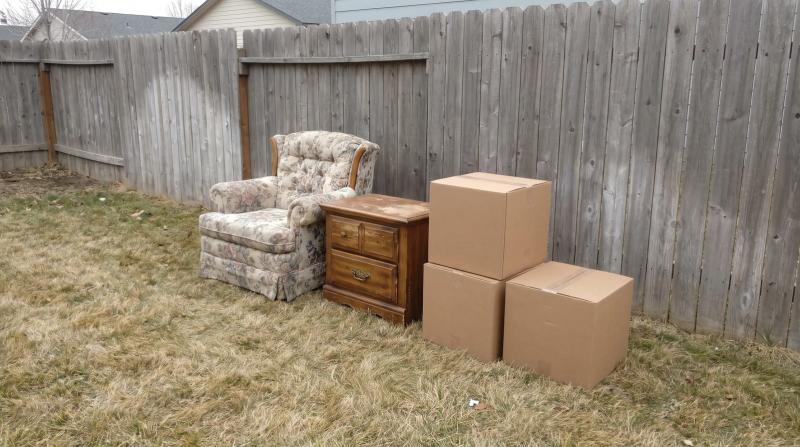 An old armchair, a wooden dresser, and sealed boxes set out on the grass for furniture removal at a rental property in Nampa, Idaho.