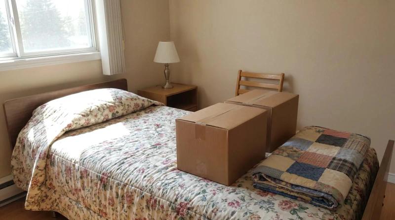 Closed moving boxes and a folded quilt on a made bed in a sunlit Boise, Idaho assisted living apartment during an estate cleanout