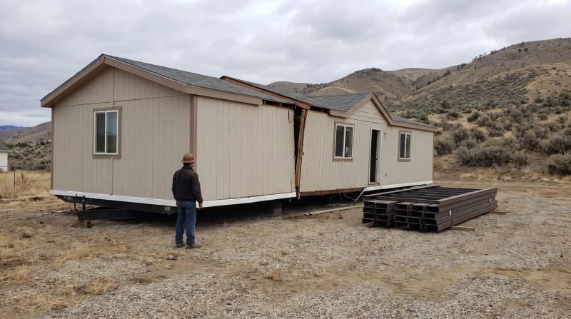 Worker beside a double wide mobile home split at the marriage line during demolition in Eagle, Idaho, with cut steel frame beams stacked nearby