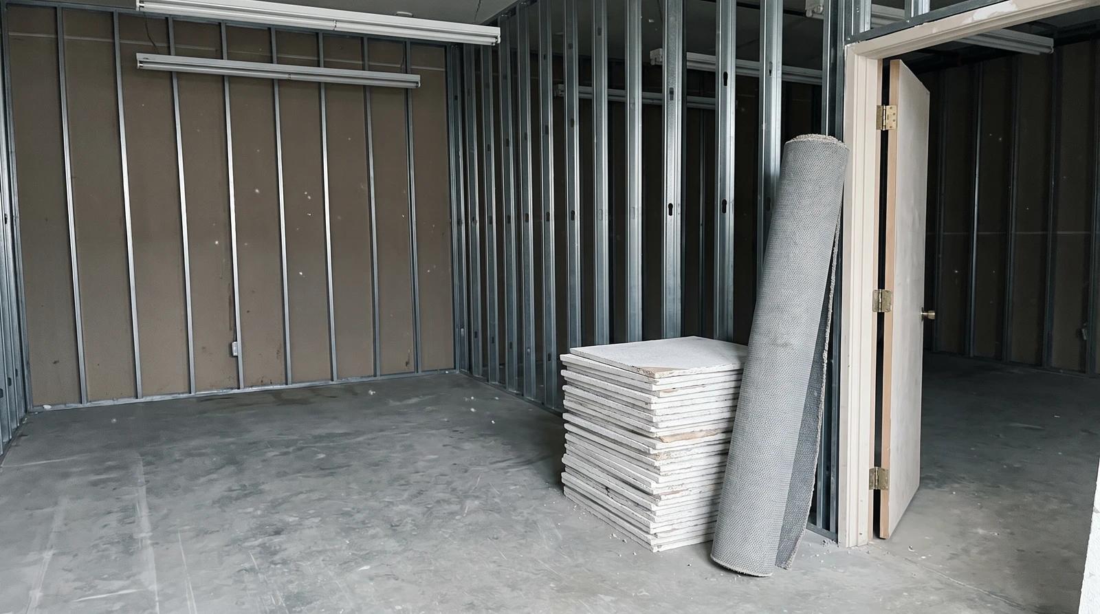 Gutted office suite with exposed metal studs, stacked ceiling tiles and rolled carpet ready for construction debris removal in Boise, Idaho