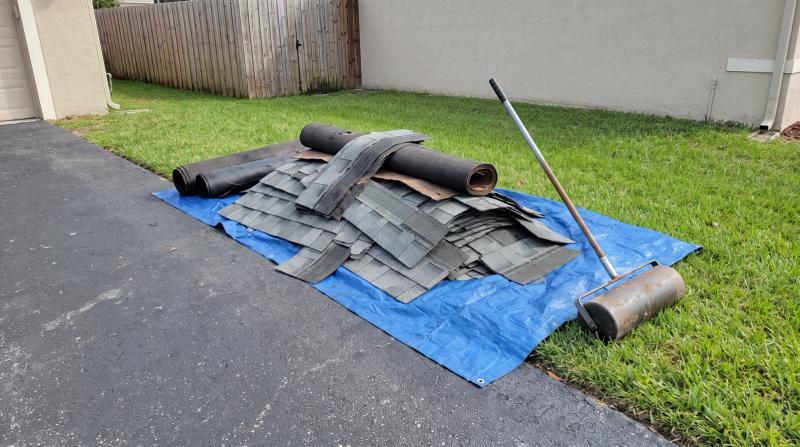 Pile of torn-off asphalt shingles on a tarp beside a driveway after a roof replacement in Nampa, Idaho, with a magnetic nail sweeper on the lawn
