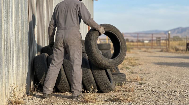 Worker in plain work clothes lifting a used tire off a stacked pile in a shop yard in Kuna, Idaho, ready for commercial tire removal