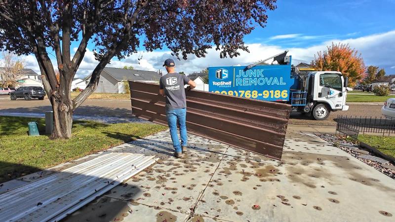 Top Shelf crew member hauling old metal siding panels to the branded truck during a new construction cleanup in a Nampa Idaho neighborhood
