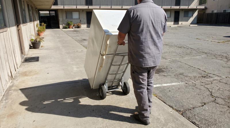 Worker moving an old refrigerator on a dolly outside an apartment building in Garden City, Idaho during bulk appliance removal