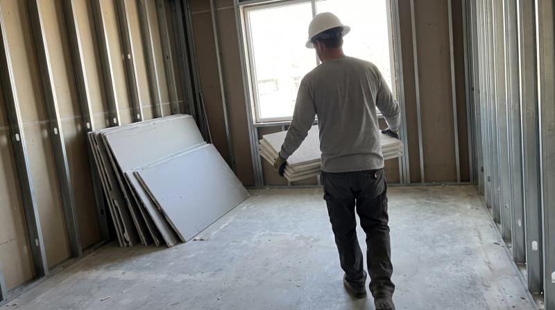 Worker carrying ceiling tiles past exposed metal studs and a pile of drywall during a commercial demolition of a leased office suite in Eagle, Idaho