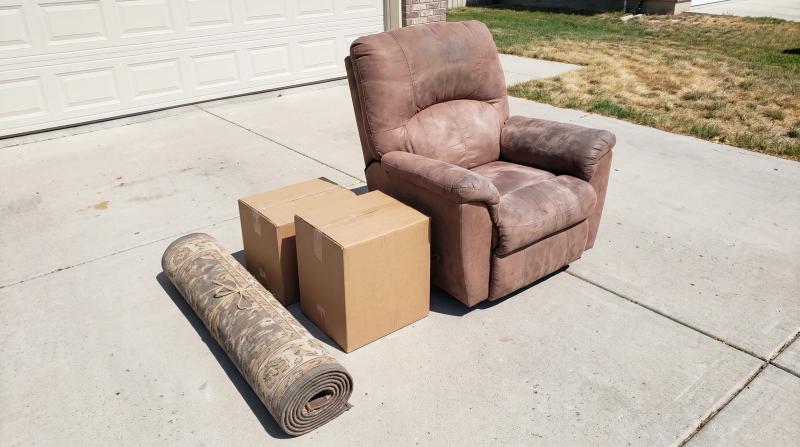 Old recliner, cardboard boxes and a rolled rug set out on a driveway in Eagle, Idaho, ready for bulk junk removal