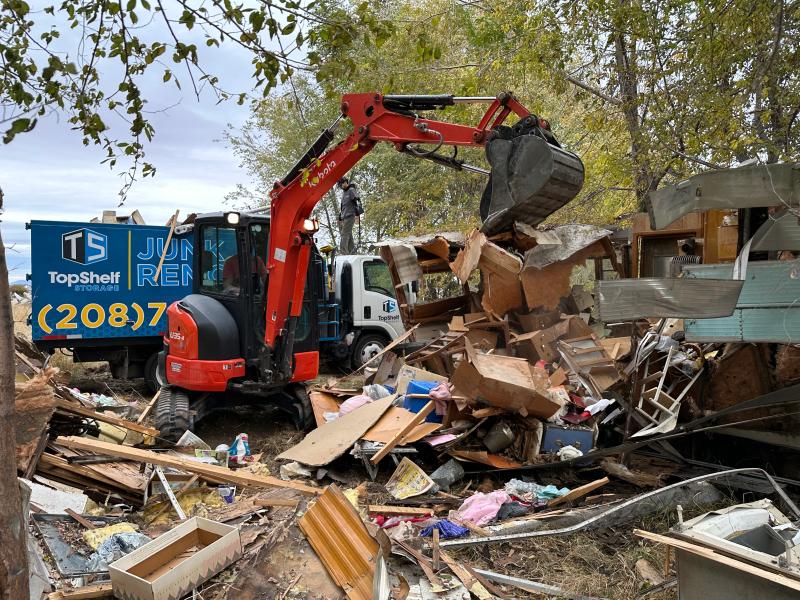 Top Shelf Kubota excavator demolishing an RV with branded truck during a demolition project in Middleton Idaho