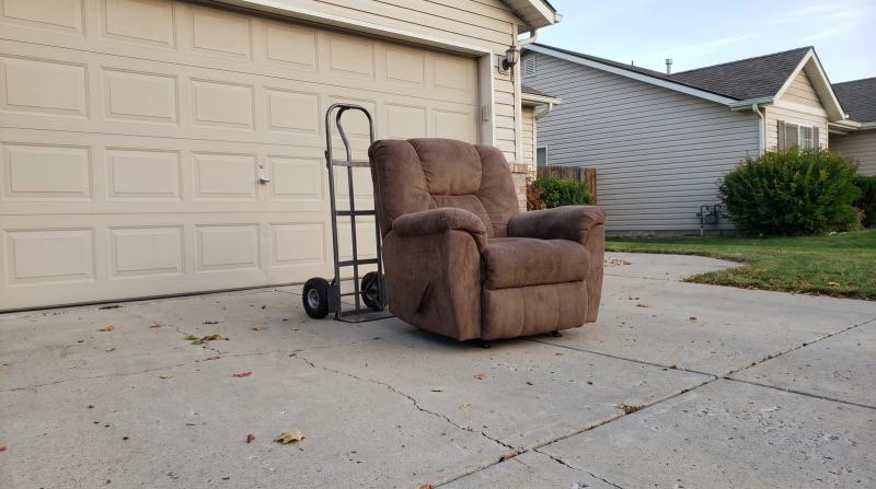 Worn recliner on a Boise driveway next to a hand dolly, waiting for single-item junk removal