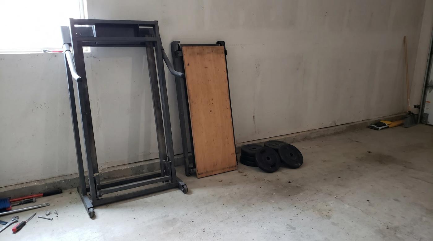 Disassembled treadmill frame leaning against a garage wall next to stacked weight plates during an exercise equipment removal job in Eagle, Idaho