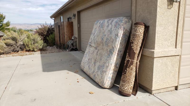 An old mattress leaning against a garage wall on a driveway in Boise, Idaho, ready for household junk removal.