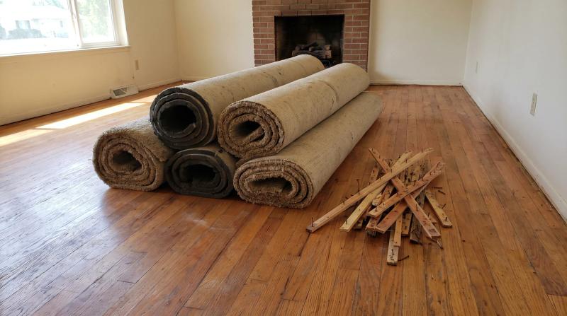 Rolled carpet and padding stacked on newly exposed oak hardwood floor after carpet removal in a Star, Idaho home