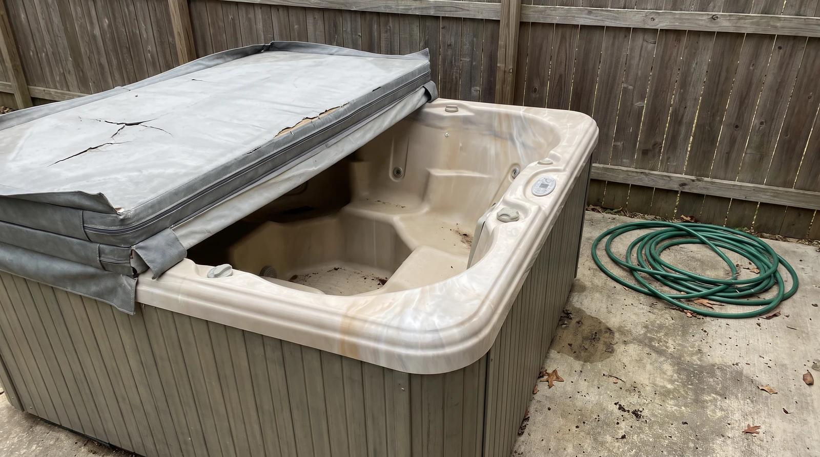 Old empty hot tub with a cracked cover on a backyard patio in Garden City, Idaho, ready for junk removal