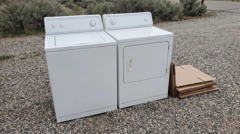 An old washer and dryer set on a gravel driveway beside stacked cardboard, waiting for appliance removal at a home in Star, Idaho.