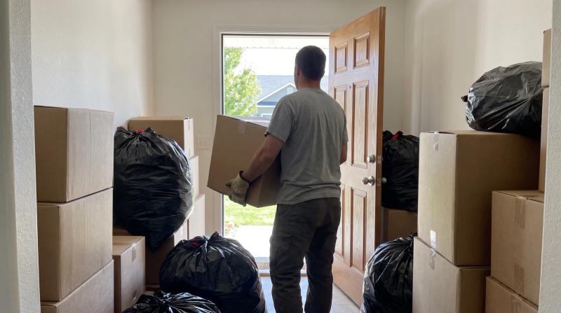 Worker carrying boxes out of a cluttered hallway during a hoarder cleanout in Meridian, Idaho