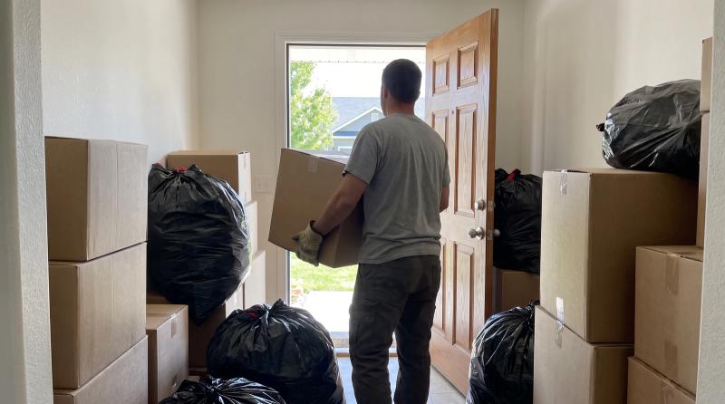 Worker carrying boxes out of a cluttered hallway during a hoarder cleanout in Meridian, Idaho