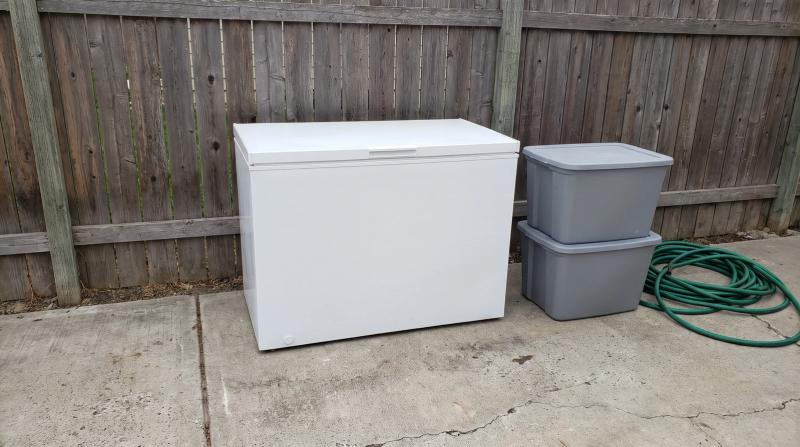 Old white chest freezer set out on a concrete driveway next to stacked storage totes at a home in Eagle, Idaho, ready for appliance removal.
