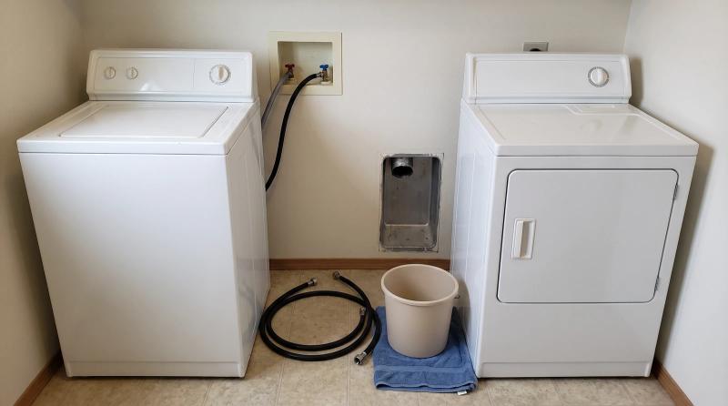 Old washer and dryer unhooked and pulled away from the wall in a Boise, Idaho laundry room, with hoses beside a bucket, ready for appliance removal