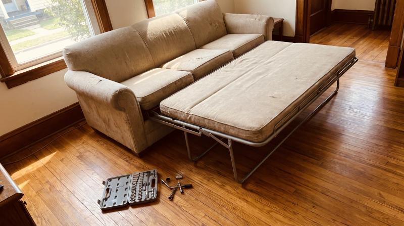 Old sleeper sofa with its fold-out steel bed partly opened before furniture removal in a Garden City, Idaho living room